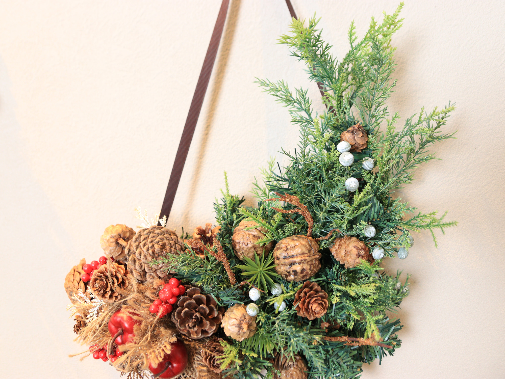 木の実とグリーンを縦長に束ねたナチュラルクリスマスの壁飾り